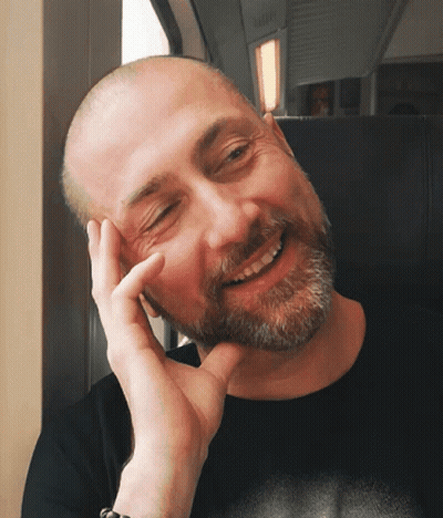 A Bald Man With A Beard Is Smiling With His Hand On His Face GIF