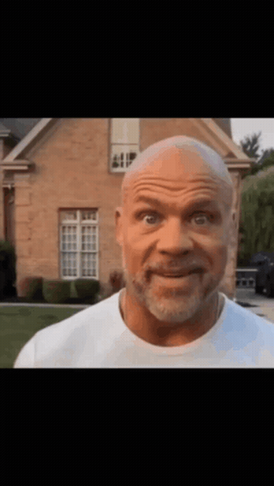 A Bald Man With A Beard Is Standing In Front Of A Brick House . GIF