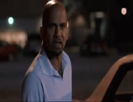 A Bald Man With A Beard Is Standing Next To A Car And Looking At The Camera . GIF