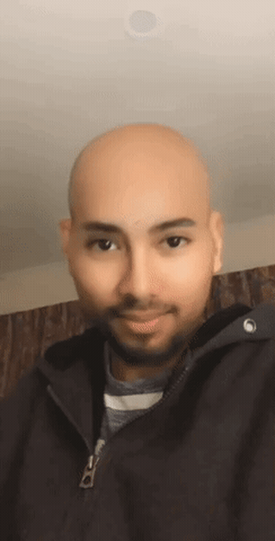 A Bald Man With A Beard Is Wearing A Black Jacket And Smiling For The Camera . GIF