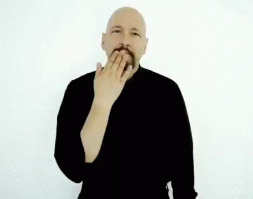 A Bald Man With A Beard Is Wearing A Black Sweater And Making A Hand Gesture . GIF