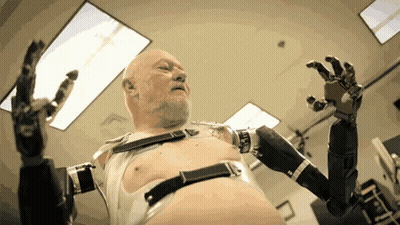 A Bald Man With A Beard Is Wearing A Robot Arm GIF