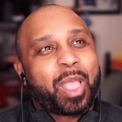 A Bald Man With A Beard Is Wearing Earbuds And Making A Funny Face . GIF