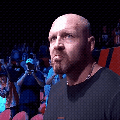 A Bald Man With A Beard Wearing A Black Shirt Stands In Front Of A Crowd With The Word Jafo On The Bottom Left GIF