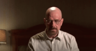 A Bald Man With A Beard Wearing Glasses Is Sitting In Front Of A Bed GIF