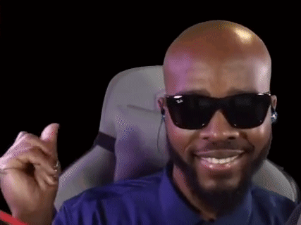 A Bald Man With A Beard Wearing Sunglasses And Headphones Is Smiling While Sitting In A Chair . GIF