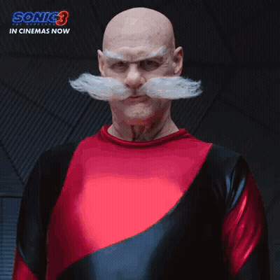 A Bald Man With A Mustache And A Red Shirt Is Standing In Front Of A Sign That Says The Robotniks GIF