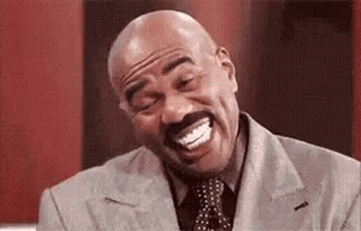 A Bald Man With A Mustache Is Laughing With His Mouth Open While Wearing A Suit And Tie . GIF