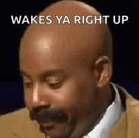 A Bald Man With A Mustache Is Wearing A Suit And Tie And Saying Wakes Ya Right Up . GIF
