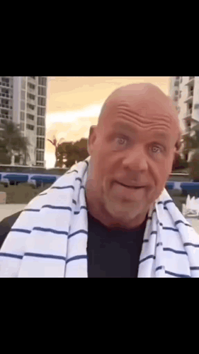 A Bald Man With A Striped Towel Around His Neck Looks At The Camera . GIF