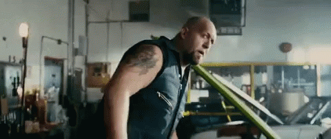 A Bald Man With A Tattoo On His Arm Is Standing In A Garage . GIF