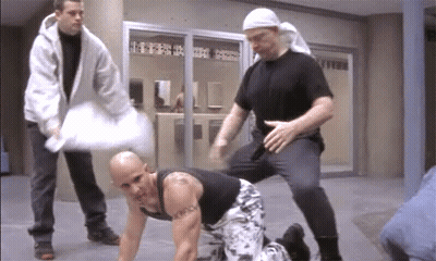 A Bald Man With A Tattoo On His Chest Is Kneeling Down GIF