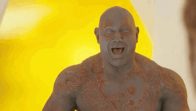 A Bald Man With A Tattoo On His Chest Is Standing In Front Of A Yellow Background . GIF