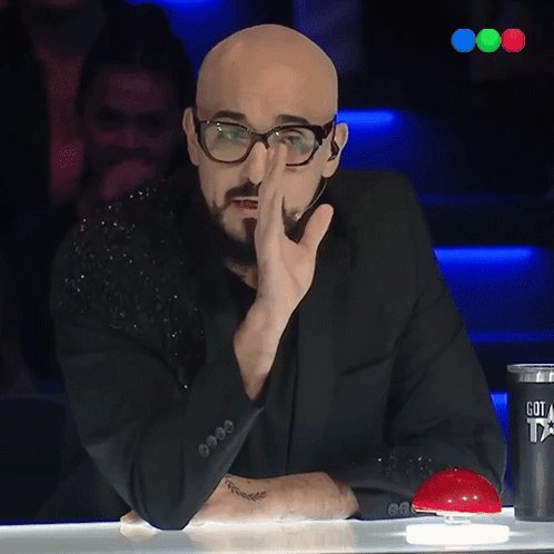 A Bald Man With Glasses And A Tattoo On His Arm Is Sitting At A Table GIF