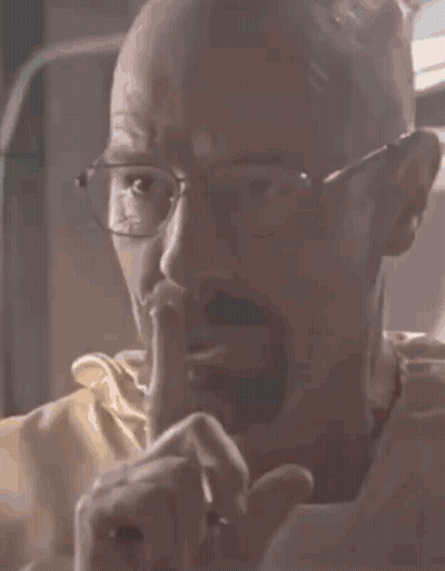 A Bald Man With Glasses Is Holding His Finger To His Mouth . GIF