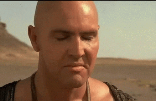 A Bald Man With His Eyes Closed Is Standing In The Desert GIF