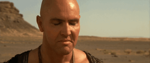 A Bald Man With His Eyes Closed Stands In A Desert GIF