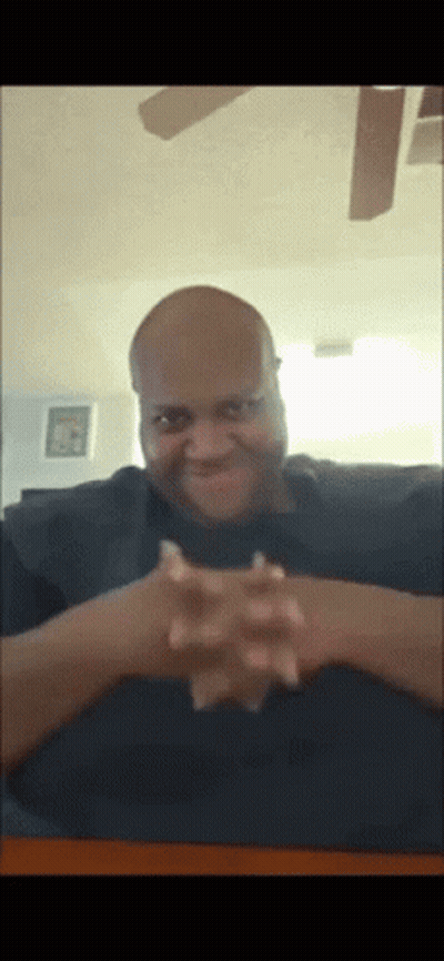 a bald man with his hands folded looks at the camera