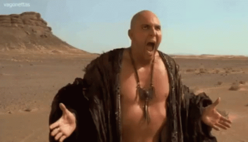 A Bald Man Without A Shirt Is In The Desert With His Mouth Open GIF