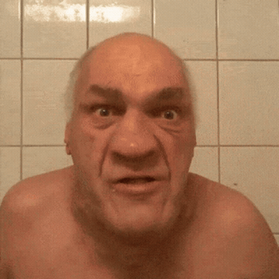 A Bald Man Without A Shirt Is Making A Funny Face In Front Of A Tiled Wall GIF