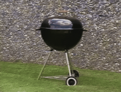 A Barbecue Grill Is Sitting On A Lawn In Front Of A Rock Wall GIF
