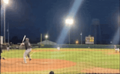 A Baseball Game Is Being Played At Night And A Batter Is Swinging His Bat GIF