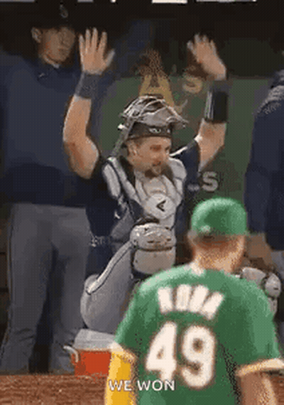 A Baseball Player In A Green Jersey Is Giving A High Five To Another Player . GIF