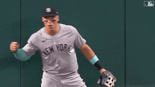 A Baseball Player In A New York Yankees Uniform Is Running On The Field With His Fist In The Air . GIF