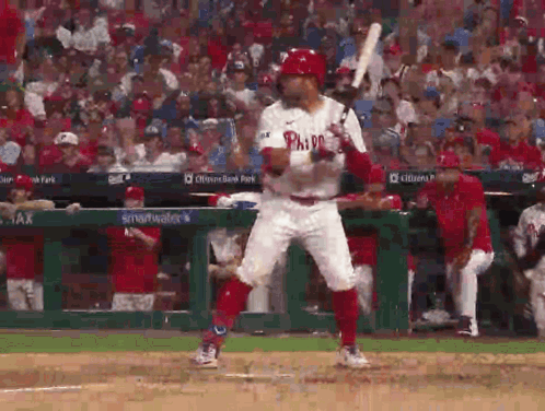 A Baseball Player In A Phillies Uniform Is Swinging A Bat At A Ball . GIF