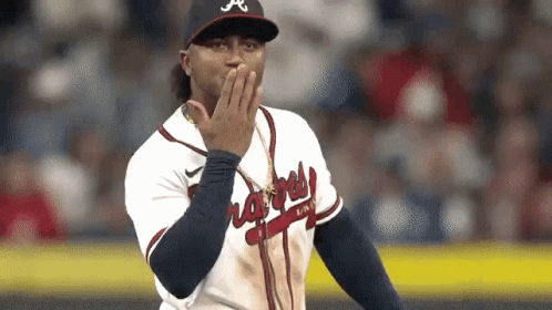 A Baseball Player Is Covering His Mouth With His Hand While Standing On A Field . GIF
