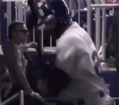 A Baseball Player Is Holding A Bat In A Stadium While A Man Looks On . GIF