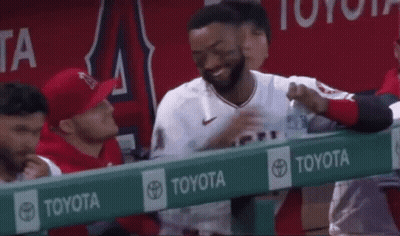 A Baseball Player Is Holding A Bottle Of Water In His Hand While Sitting In The Dugout . GIF