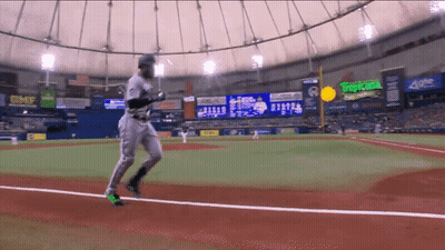 A Baseball Player Is Running On The Field In Front Of A Scoreboard That Says Tropicana On It GIF