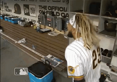 A Baseball Player Is Standing In A Dugout With A Blue Cooler GIF