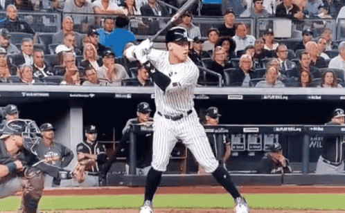 A Baseball Player Is Swinging A Bat At A Ball In Front Of A Crowd Of People . GIF