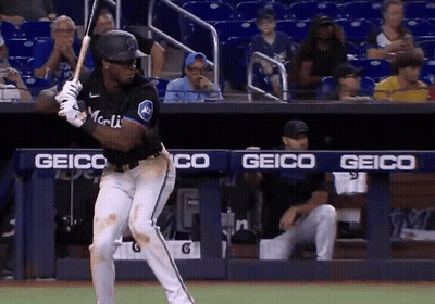 A Baseball Player Is Swinging At A Ball In Front Of A Geico Banner GIF