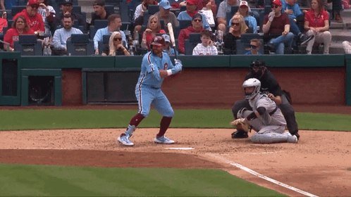 A Baseball Player Is Swinging His Bat At A Ball While A Catcher Watches GIF