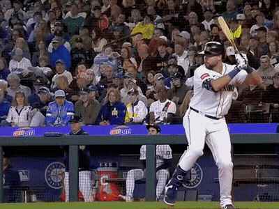 A Baseball Player Swings His Bat At A Ball In Front Of A Crowd With A Banner That Says Coca Cola GIF