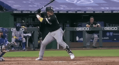 A Baseball Player Swings His Bat At A Ball In Front Of A Geico Sign GIF