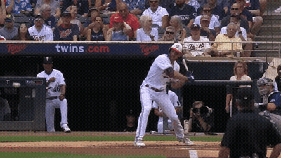A Baseball Player Swings His Bat At A Ball In Front Of A Twins.com Banner GIF