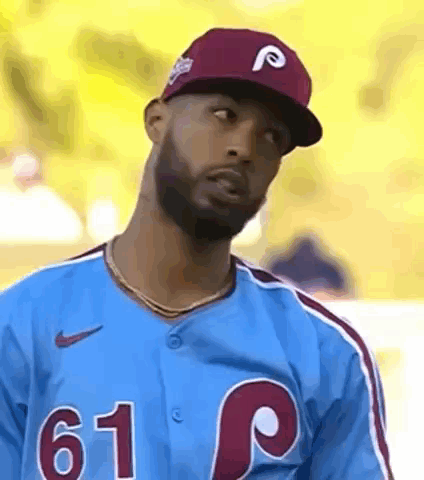 A Baseball Player Wearing A Blue Jersey And A Red Hat Is Looking At The Camera . GIF