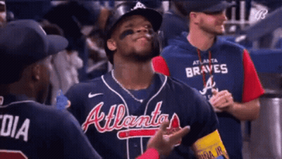 A Baseball Player Wearing A Braves Jersey Is Standing In The Dugout Talking To His Teammates . GIF