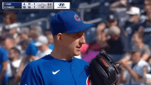 A Baseball Player Wearing A Cubs Hat Stands In Front Of A Scoreboard GIF