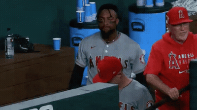A Baseball Player Wearing A Gray Angels Jersey Is Sitting In The Dugout . GIF
