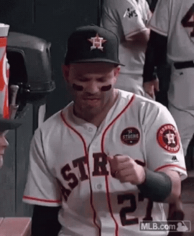 A Baseball Player Wearing A Hat And A Jersey Is Sitting On A Bench In The Dugout . GIF