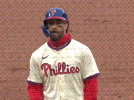 A Baseball Player Wearing A Helmet And A Phillies Jersey Is Standing On A Field . GIF