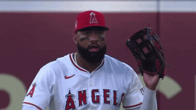 A Baseball Player Wearing A Red Hat And A White Jersey With The Word Angels On It Is Holding A Glove In His Hand . GIF
