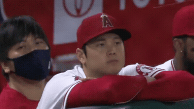 A Baseball Player Wearing A Red Hat And A White Shirt Is Sitting In The Dugout With His Arms Crossed . GIF