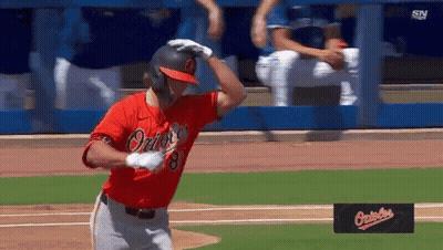 A Baseball Player Wearing A Red Orioles Jersey Is Standing On The Field GIF