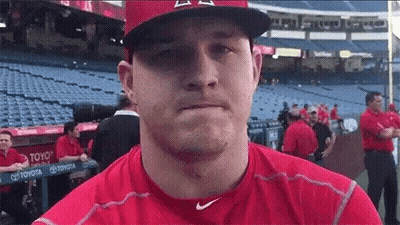 A Baseball Player Wearing A Red Shirt And A Hat Is Standing In A Dugout . GIF